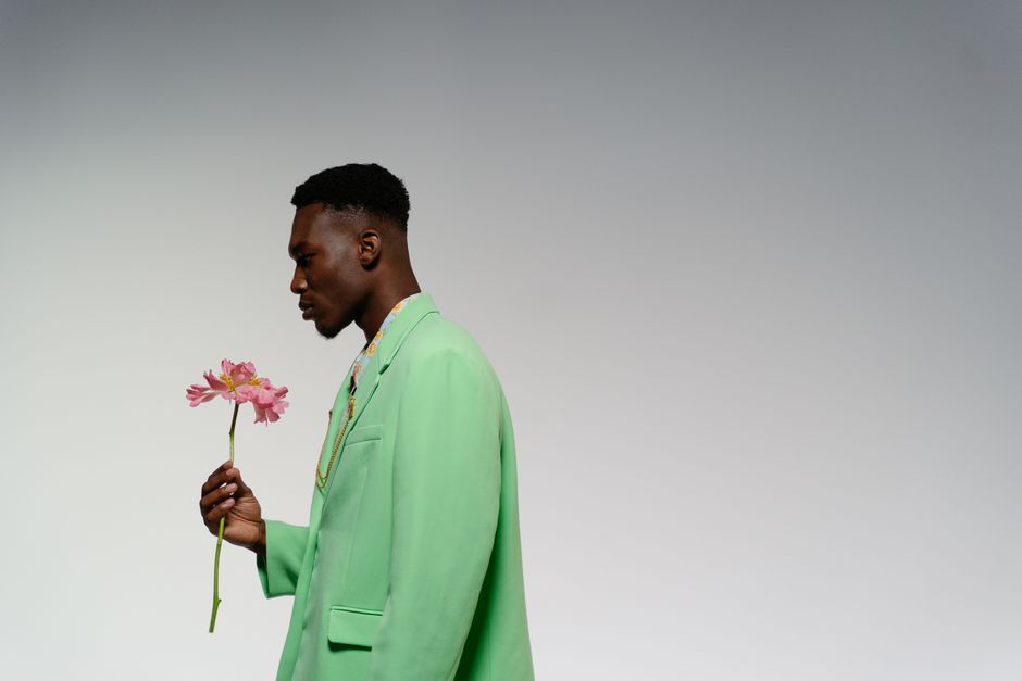 Perfil de un hombre con traje verde sosteniendo una flor rosa en un entorno de estudio.