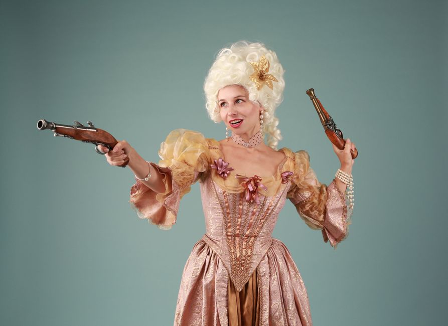 Una joven en traje barroco posa sosteniendo pistolas de percusión, exudando elegancia y encanto histórico.