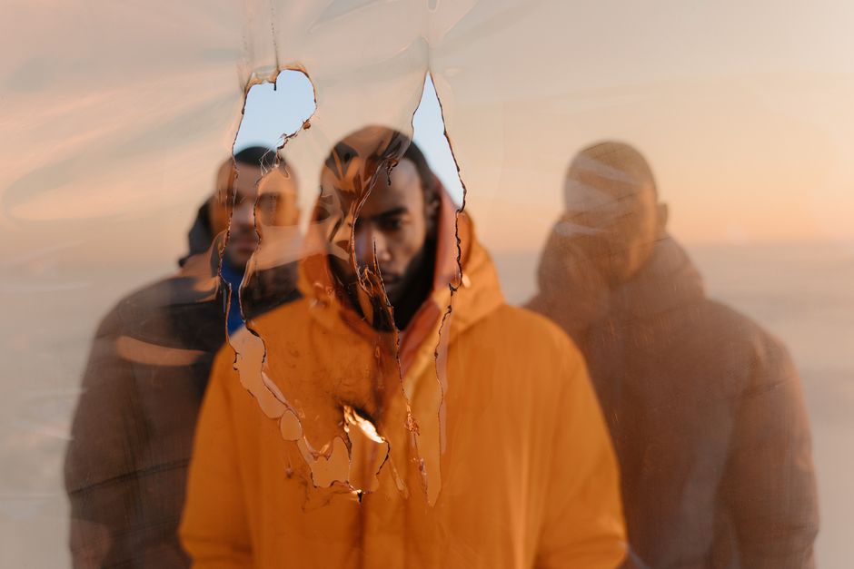 Tres hombres con chaquetas acolchadas vistos a través de vidrio quemado en un entorno nevado durante la puesta de sol, creando un efecto dramático.
