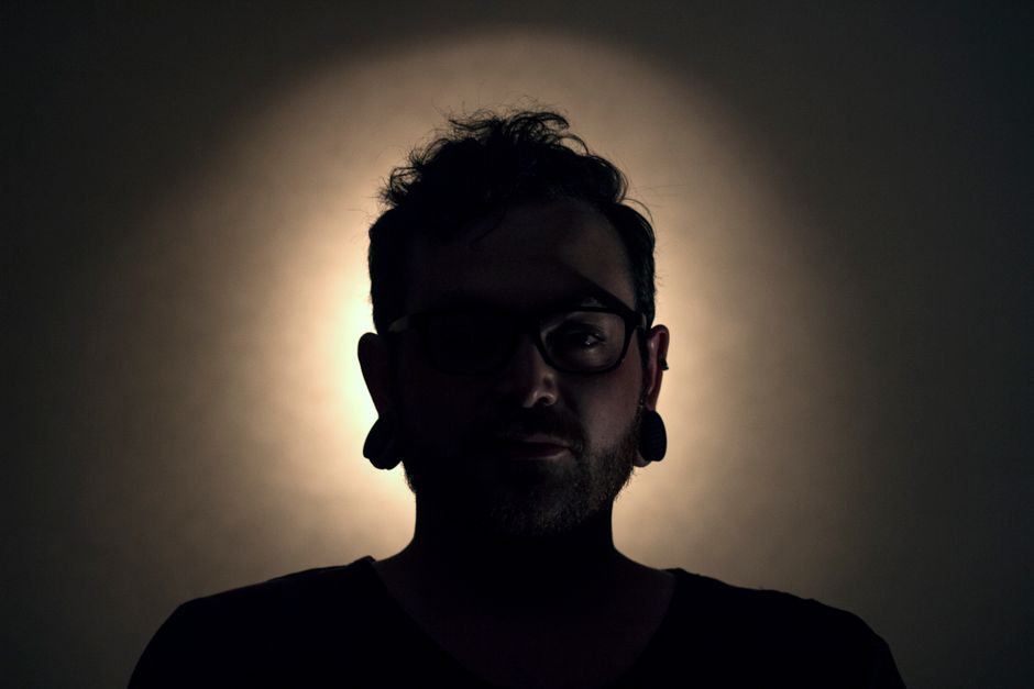 Silueta de un hombre de perfil con túneles en las orejas, retroiluminado con una iluminación dramática.