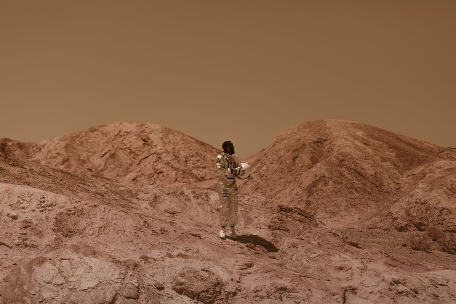 Un hombre con un traje espacial se encuentra en un paisaje desértico y árido, evocando una sensación de exploración.