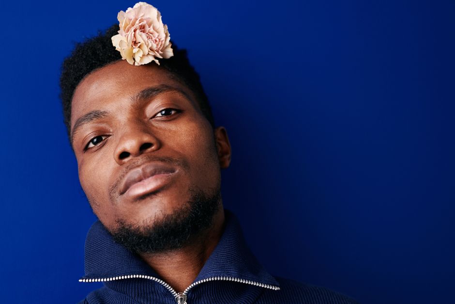 Retrato en primer plano de un hombre elegante con un clavel rosa, fondo azul.