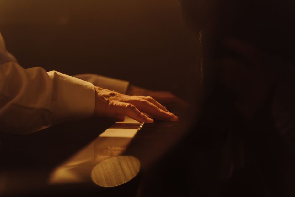 Una vista en primer plano de una mano tocando un piano con luz cálida, capturando la emoción musical.