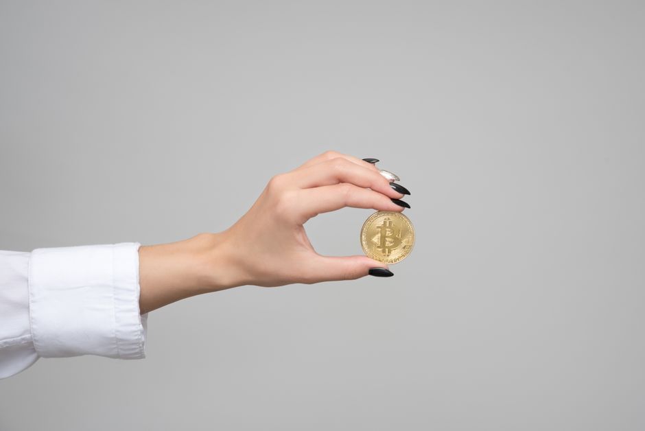 Primer plano de la mano de una mujer sosteniendo una moneda de bitcoin contra un fondo neutro.
