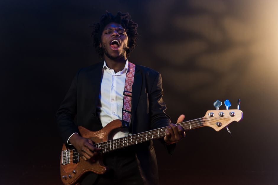 Un músico negro actuando con pasión en el escenario bajo las luces, tocando un bajo.