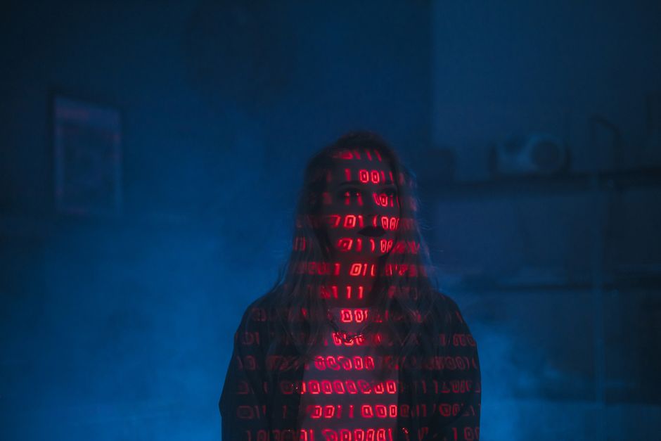 Una silueta misteriosa con código binario rojo proyectado sobre la cara, con un fondo oscuro y sombrío.