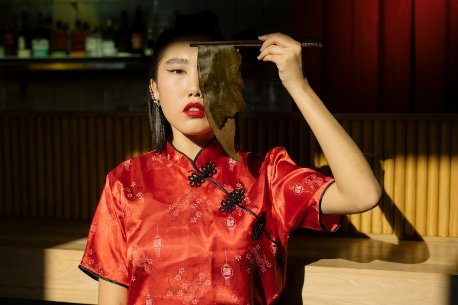 Mujer elegante con un vestido tradicional rojo sosteniendo algas con palillos en el interior.