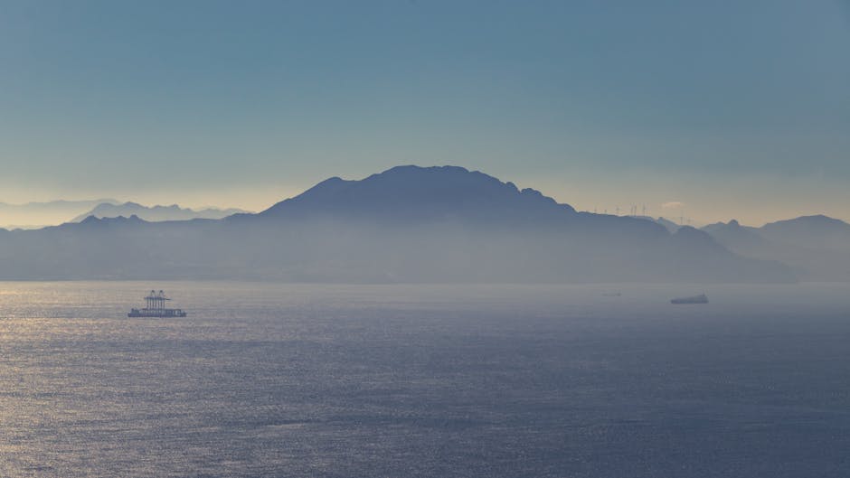 Vista serena del mar y las montañas distantes cerca de Gibraltar durante el día, con barcos visibles en el horizonte.