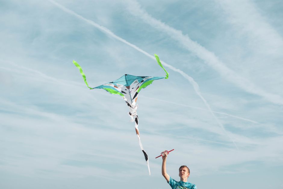 Un joven con una camisa azul volando una cometa colorida en un cielo despejado, disfrutando de la brisa.