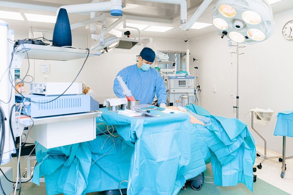 Médico en traje quirúrgico realizando una operación en una sala de operaciones bien equipada.