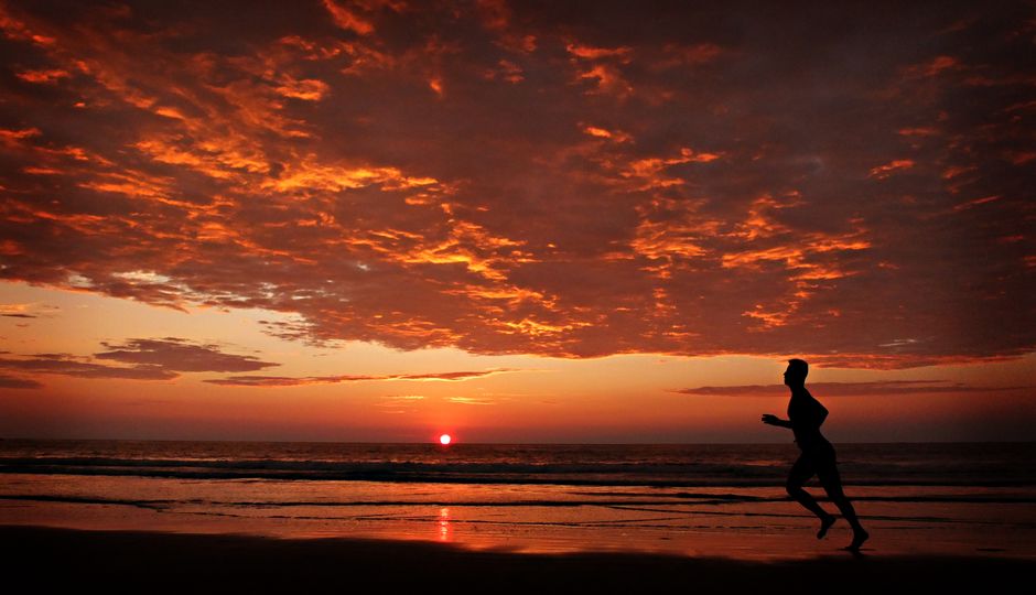 Una persona corre por una playa ecuatoriana durante una vibrante puesta de sol, creando una silueta impresionante.