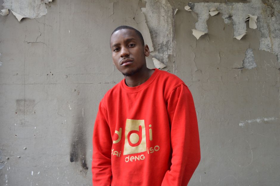 Joven posando con confianza en una sudadera roja frente a una pared de concreto urbano.