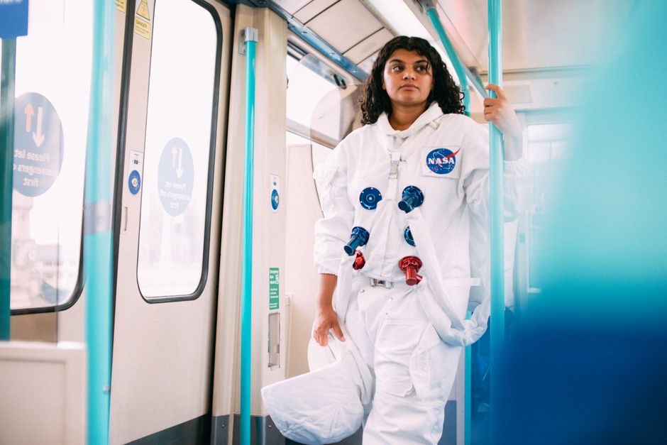 Una mujer con un disfraz de astronauta en un tren público, combinando ciencia ficción con el trayecto diario.
