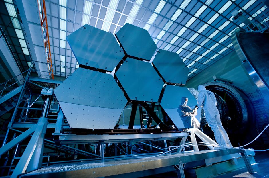 Ingenieros en trajes de protección trabajan en espejos telescópicos en un laboratorio de alta tecnología.