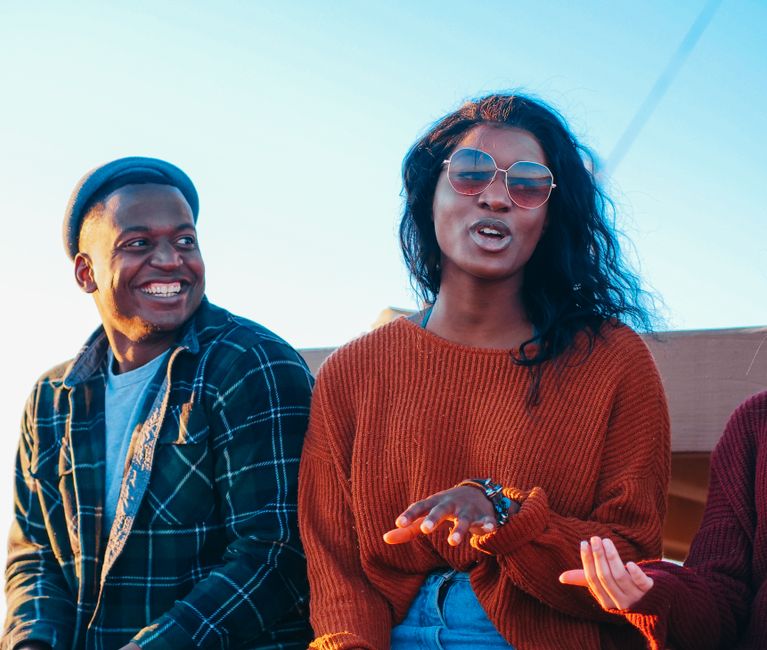Amigos felices sentados al aire libre, compartiendo sonrisas y conversación bajo el sol.
