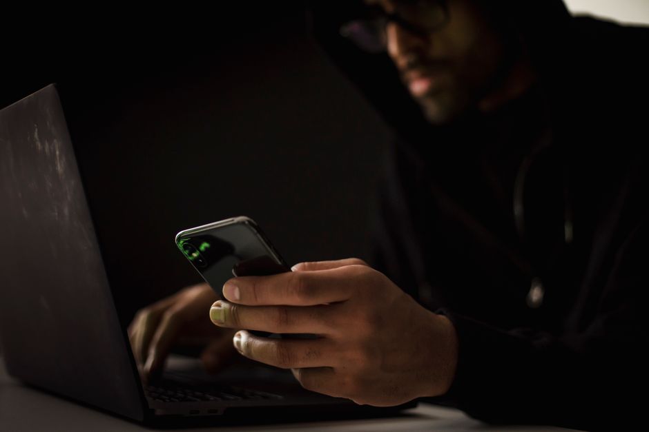 Hacker étnico De Cultivos Con Smartphone Escribiendo En La Computadora Portátil En Una Habitación Oscura