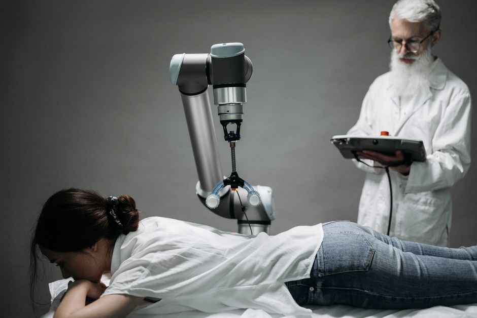 Una mujer recibe un masaje robótico mientras un científico monitorea, mostrando la tecnología moderna.