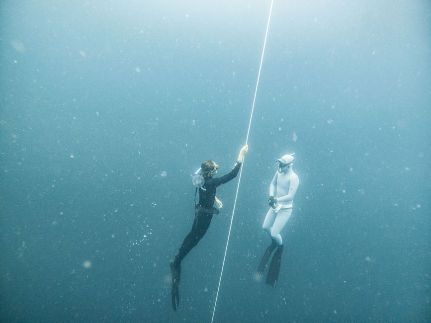 Dos apneístas suspendidos en las profundas aguas azules de Lombok, Indonesia, mostrando la exploración submarina.