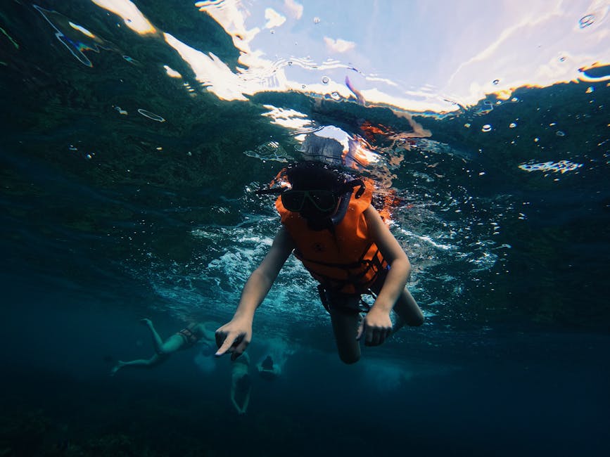 Un niño haciendo snorkel en las cristalinas aguas azules de Satun, Tailandia, vistiendo un chaleco salvavidas naranja.