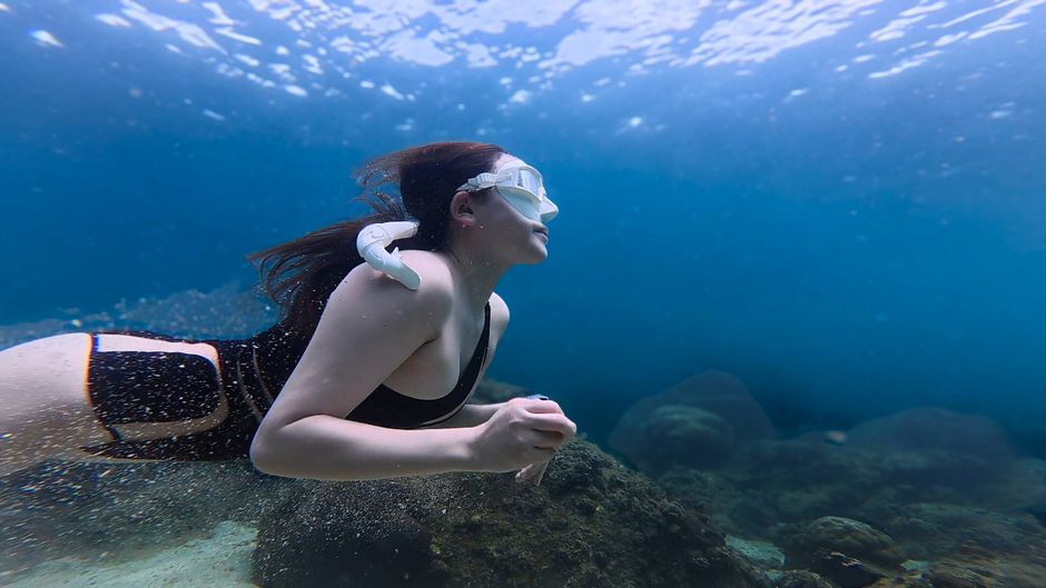 Una mujer practica snorkel bajo el agua en el océano claro, explorando la vida marina.