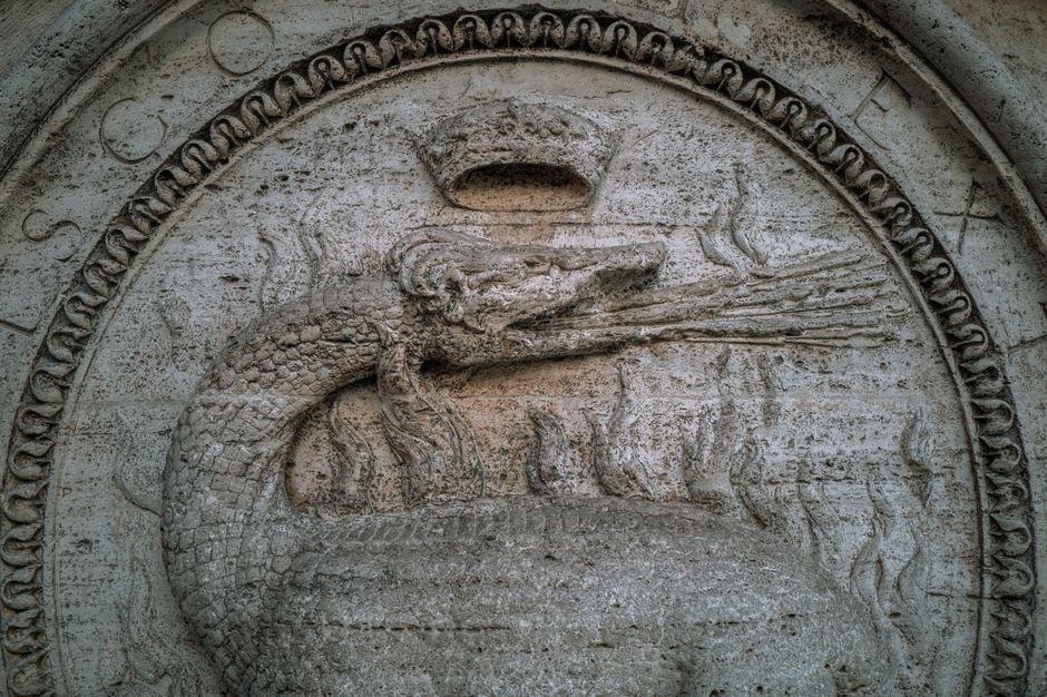 Primer plano de un relieve de piedra detallado que representa un dragón en un monumento histórico de Roma.