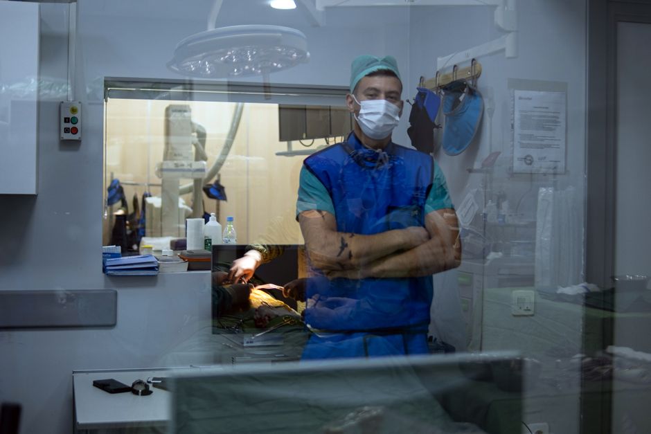 Cirujano con uniforme quirúrgico observando a través de una ventana de cristal durante un procedimiento médico.