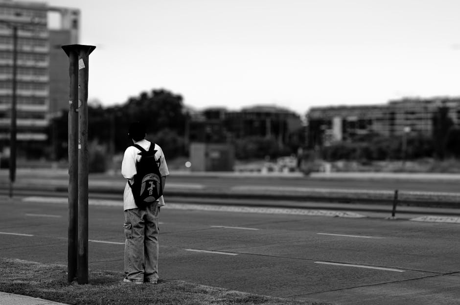 Una figura solitaria con una mochila se encuentra en una calle urbana, creando una escena urbana melancólica.