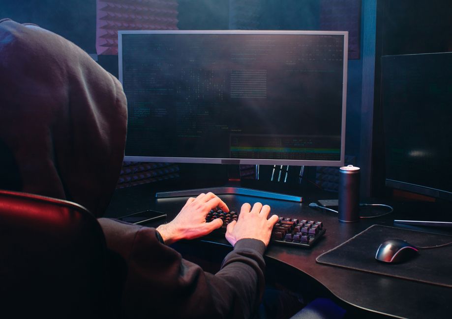 Una persona con sudadera se sienta frente a una pantalla de computador, involucrada en actividades de codificación o hacking.