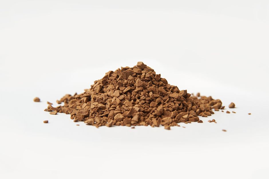 Una imagen en primer plano de gránulos de café instantáneo marrones sobre un fondo blanco.