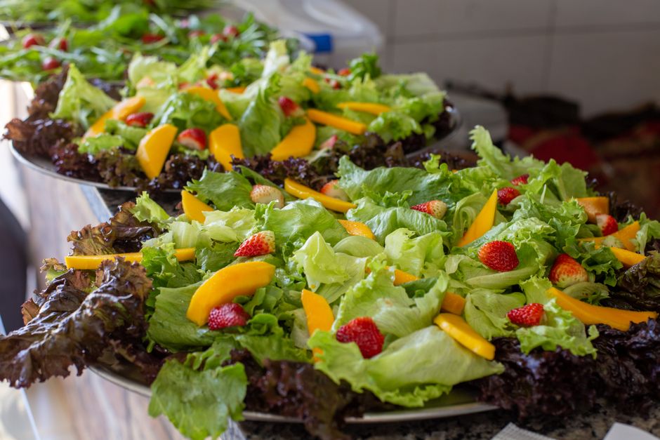 Primer plano de una bandeja de ensalada de frutas frescas y lechuga con fresas vibrantes y rodajas de mango.