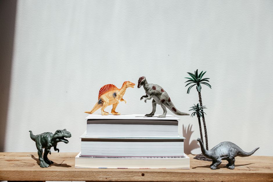 Juguetes vibrantes de dinosaurios organizados en pilas de libros sobre un fondo sencillo, creando una escena divertida.