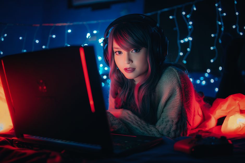 Joven mujer con auriculares, jugando en una laptop rodeada de luces de ensueño. Ambiente acogedor.