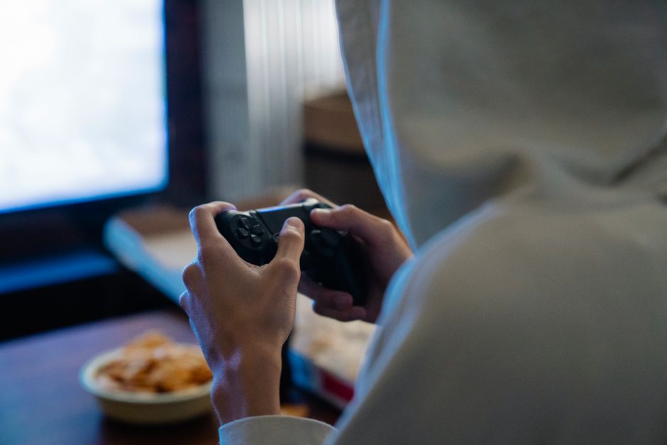 Un joven adulto con sudadera está jugando a un videojuego en una consola en casa para relajarse.