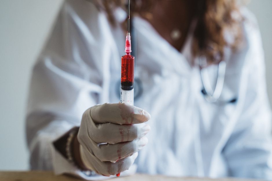 Un médico con guantes sostiene una jeringa llena de líquido rojo, enfatizando el cuidado médico.