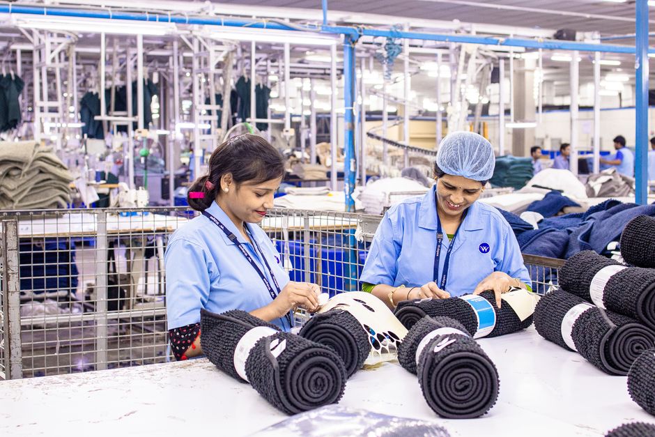 Dos trabajadoras textiles procesan rollos de tela en un entorno industrial muy animado.