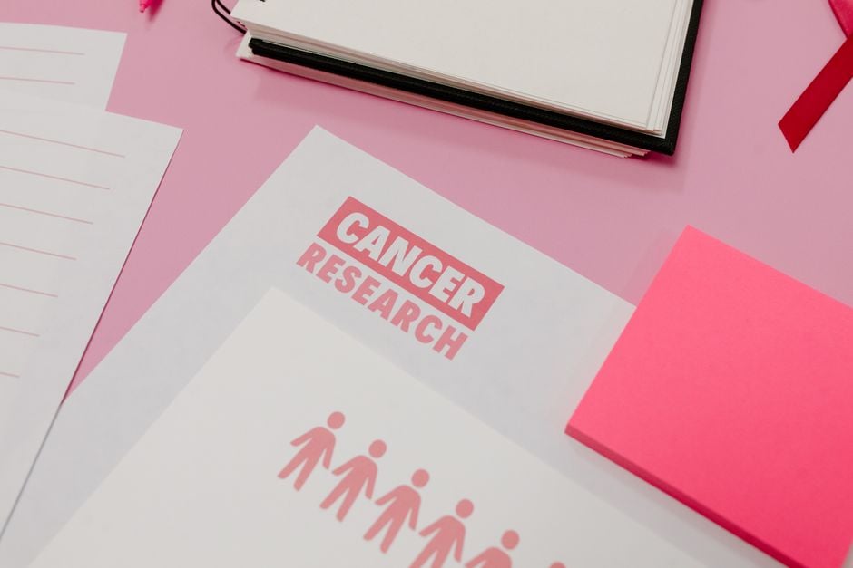 Materiales de investigación sobre el cáncer dispuestos en un escritorio rosa. Espacio de trabajo profesional.