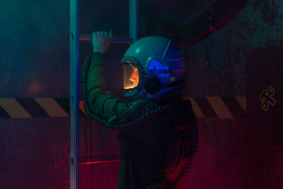 Una astronauta mujer en un traje espacial explora un entorno futurista en el interior. La iluminación tenue realza la atmósfera de ciencia ficción.