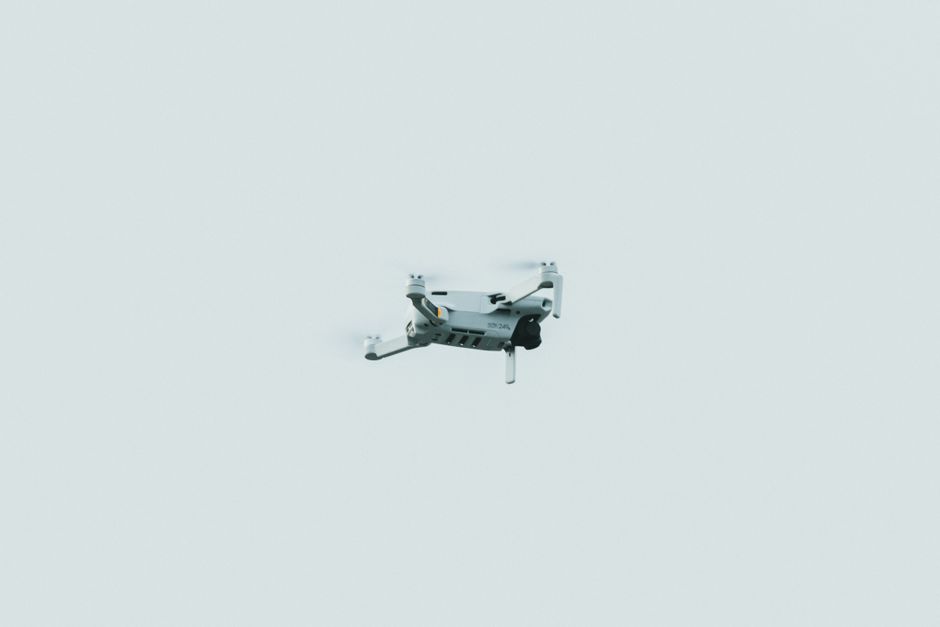 Un solo drone volando contra un cielo claro y pálido en una composición minimalista.