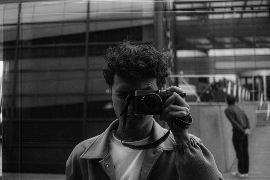 Autorretrato en blanco y negro de un fotógrafo reflejando en una ventana de la ciudad.