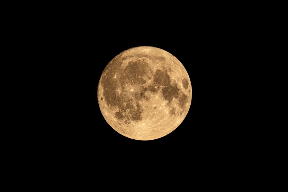 Foto de la luna llena que muestra cráteres y detalles contra un oscuro cielo nocturno.