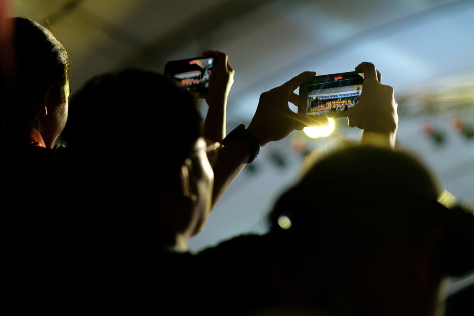 Siluetas de personas usando smartphones para grabar un evento en vivo en interiores.