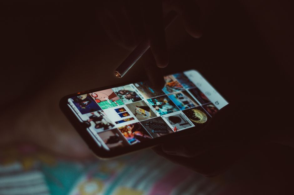 Acercamiento de una mano sosteniendo un smartphone y un cigarrillo, navegando por imágenes.