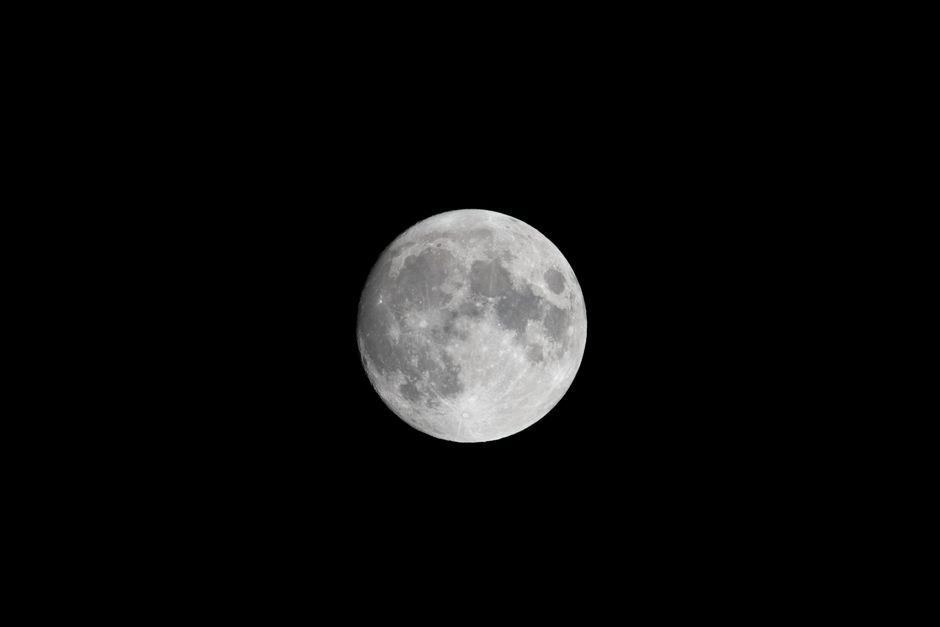 Vista cercana de la luna llena contra un oscuro cielo nocturno, mostrando detalles lunares.