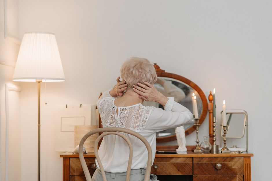 Mujer sentada ante un espejo vintage, sosteniendo su cabello hacia arriba. La escena transmite un ambiente cálido y relajado.