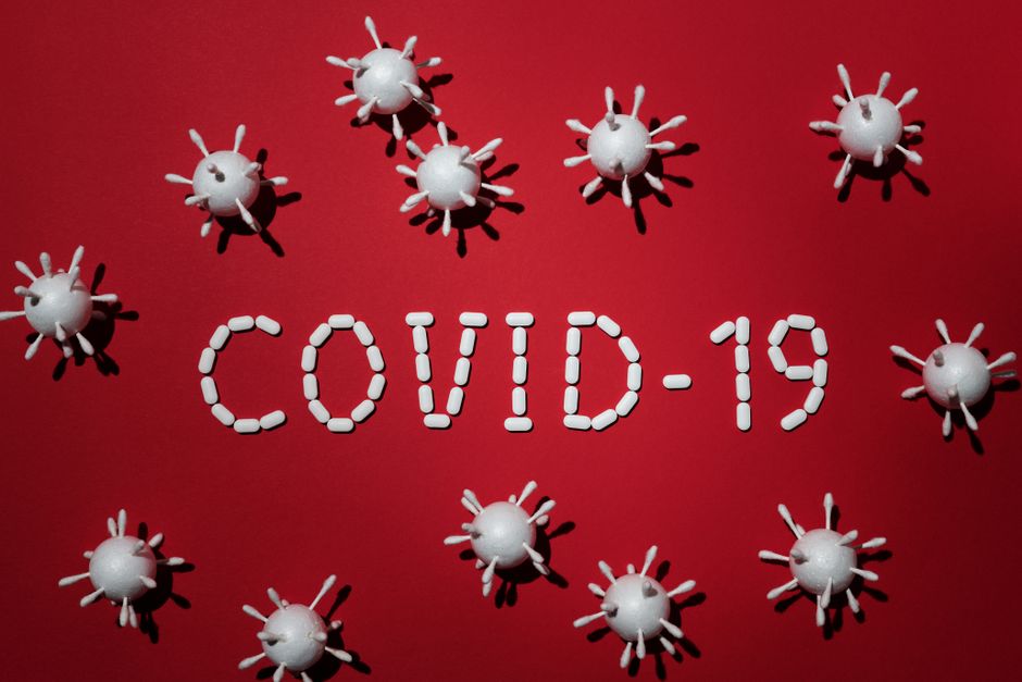 Representación creativa del COVID-19 utilizando pastillas y modelos de virus sobre un fondo rojo.