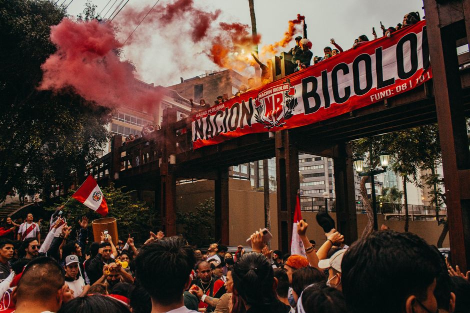 Una escena de protesta dinámica en Lima con una multitud reunida bajo un cielo lleno de humo rojo.