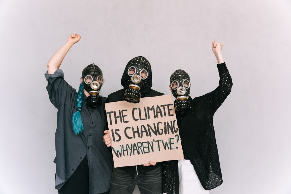 Tres activistas con mascarillas de gas sostienen un cartel de protesta sobre el cambio climático en un interior.