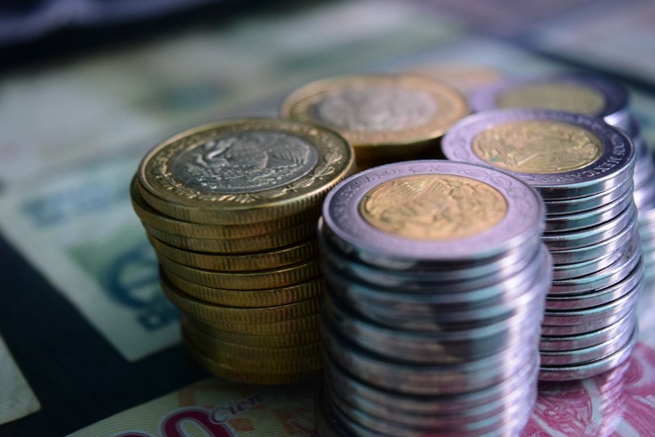 Primer plano de montones de monedas de oro y plata sobre varios billetes, simbolizando riqueza y ahorros.