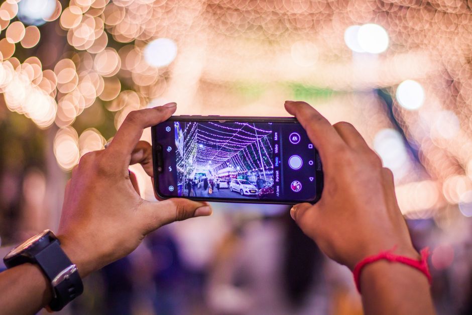 Manos sosteniendo un smartphone para tomar una foto de luces festivas en una calle de Kolkata.