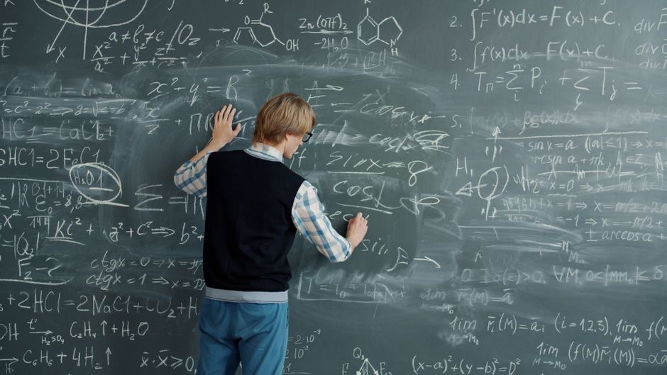 Un joven adulto escribiendo fórmulas matemáticas en una pizarra.